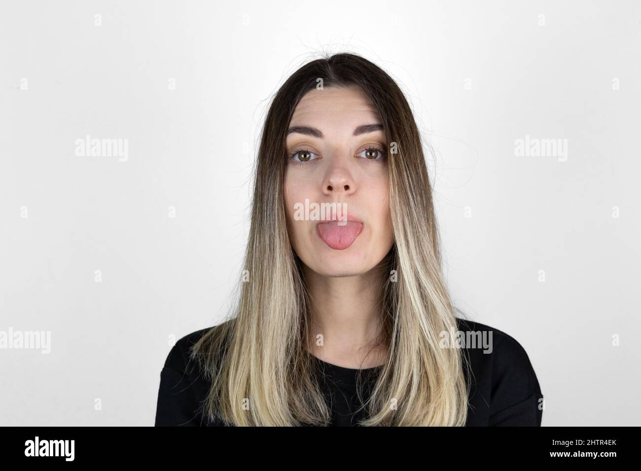 Young woman sticking out tounge, close up portrait. Teasing you through camera while isolated with white background. Stock Photo