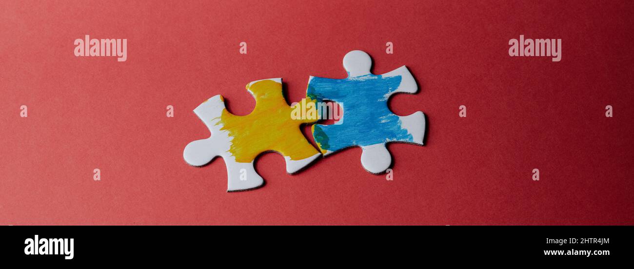 high angle view of two jigsaw pieces painted with the colors of the ukrainian flag on a red background, in a panoramic format to use as web banner or Stock Photo