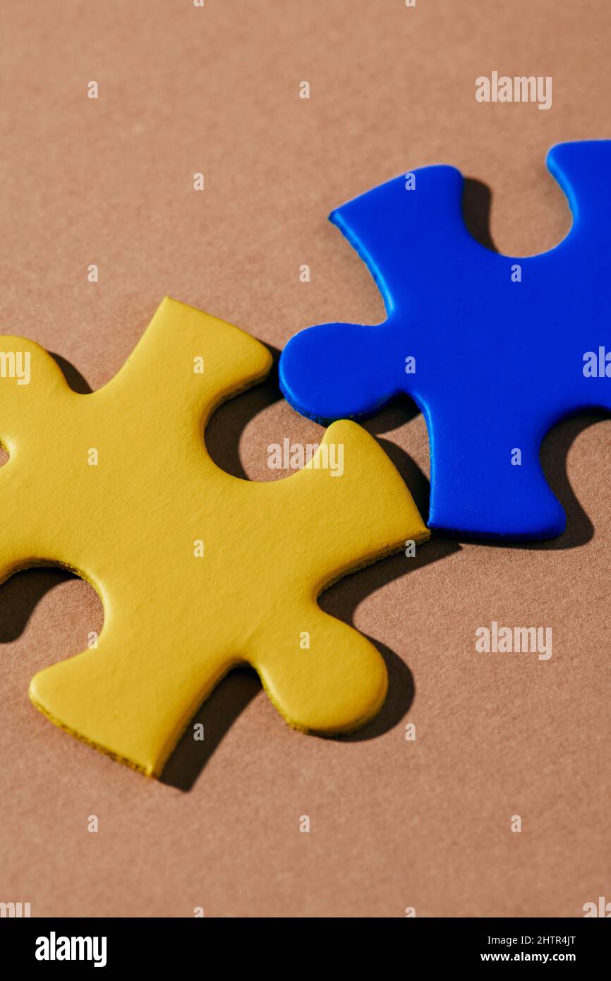 closeup of two puzzle pieces, with the colors of the ukrainian flag, on a brown background Stock Photo