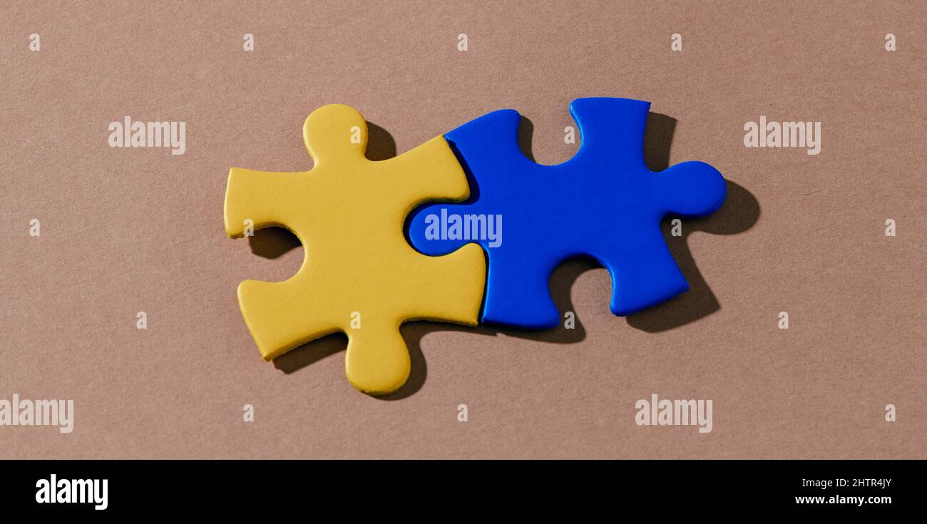 high angle view of two puzzle pieces painted in yellow and blue forming the ukrainian flag on a brown background, in a panoramic format to use as web Stock Photo
