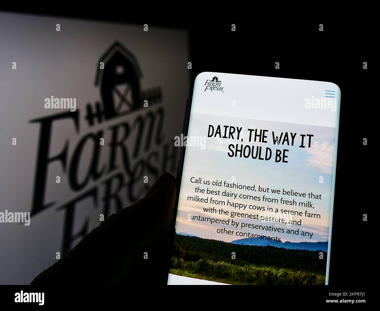 Person holding smartphone with website of Malaysian dairy company Farm