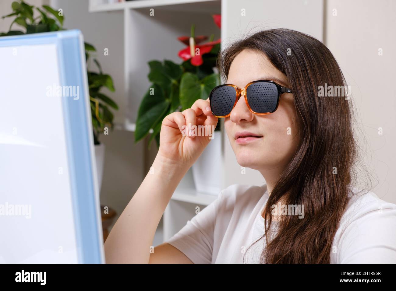 A woman looks at a computer screen through perforated glasses with