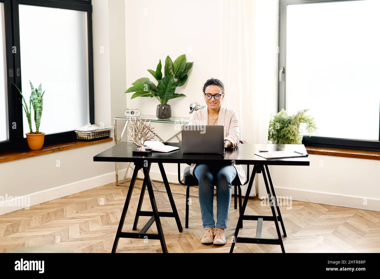 Concentrated young office worker businesswoman in glasses sitting at the desk in the office, working on a laptop Stock Photo