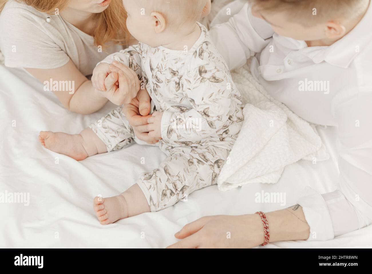 Top view of young family in white clothes sitting on white cotton bed linen with cute little blue-eyed baby infant. Stock Photo