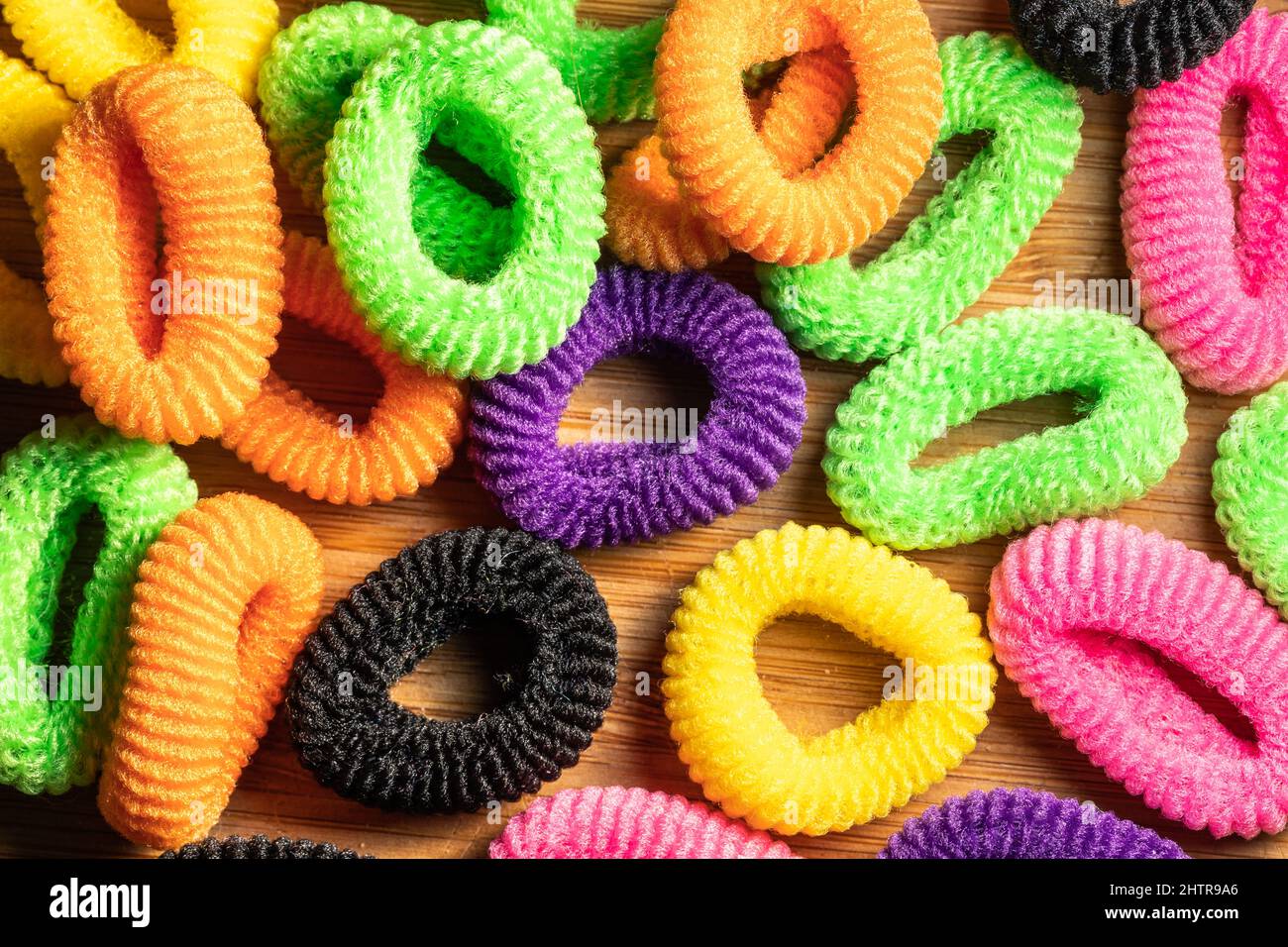 Lots of multi-colored hair elastic bands tied together with crunchies. Hair care and fashion. Multicolored hair accessories, isolated objects on woode Stock Photo