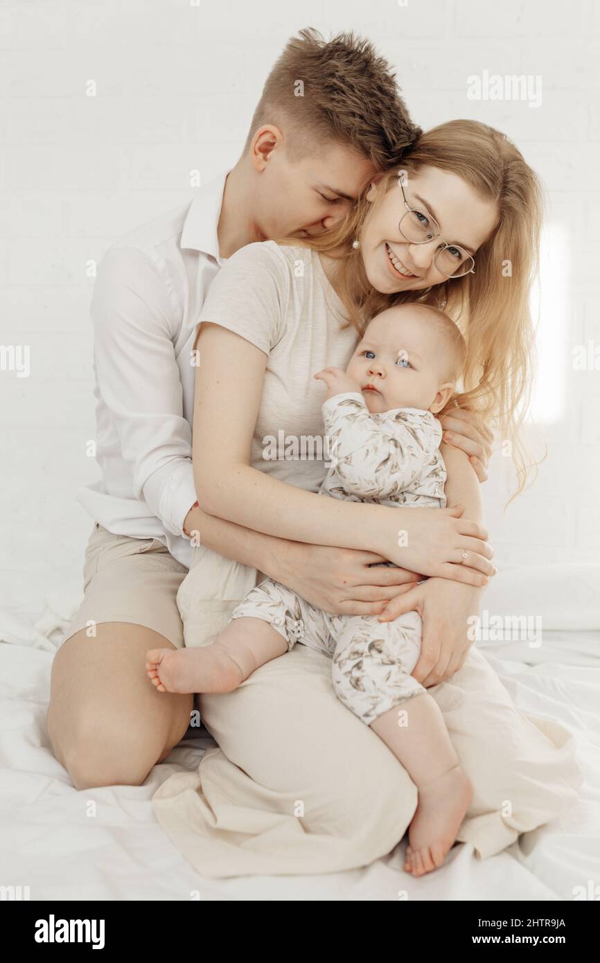 Portrait of young happy smiling family in white clothes with awesome little plump blue-eyed baby infant toddler sitting. Stock Photo
