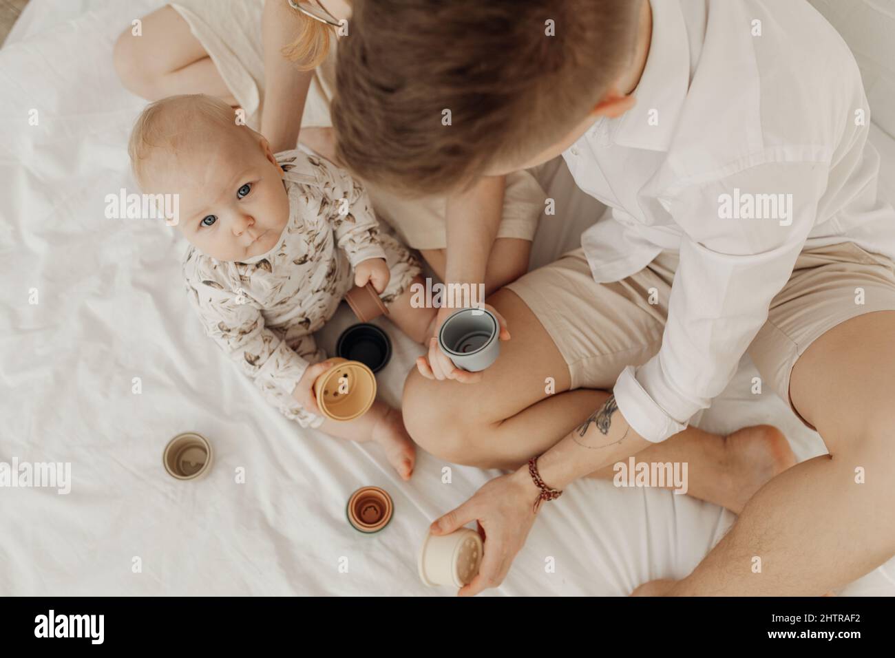 Top view of young man and unrecognizable woman holding silicone bowls of different size with little plump infant baby. Stock Photo