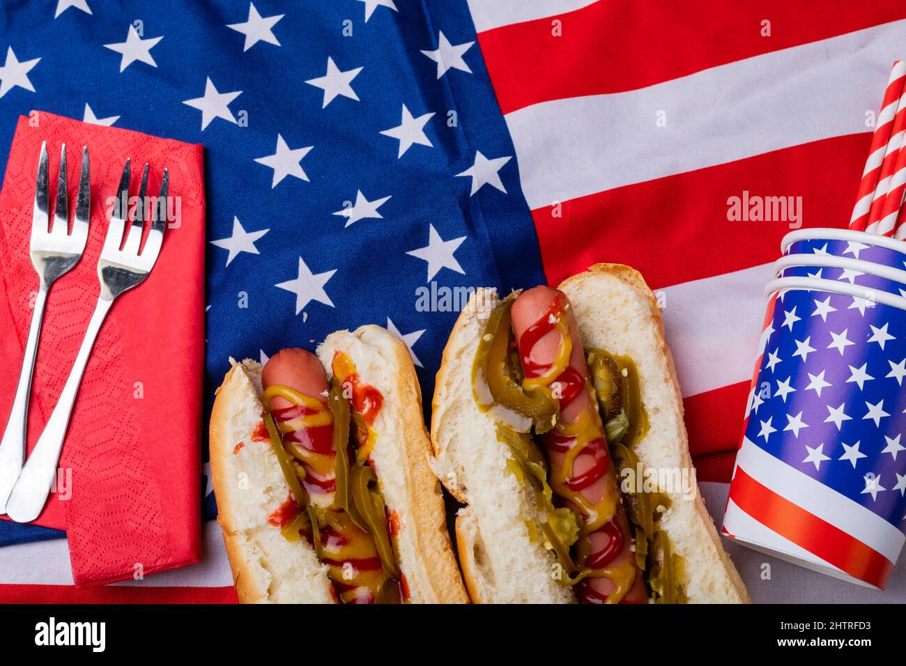 Overhead view of hot dogs with jalapeno served on american flag with fork and disposable cups Stock Photo