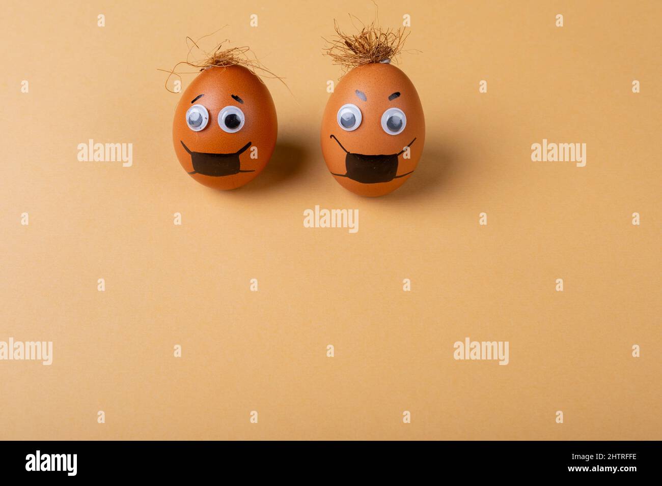 Doodle eyes, eyebrow and mask drawing on easter eggs with strings on top against orange background Stock Photo
