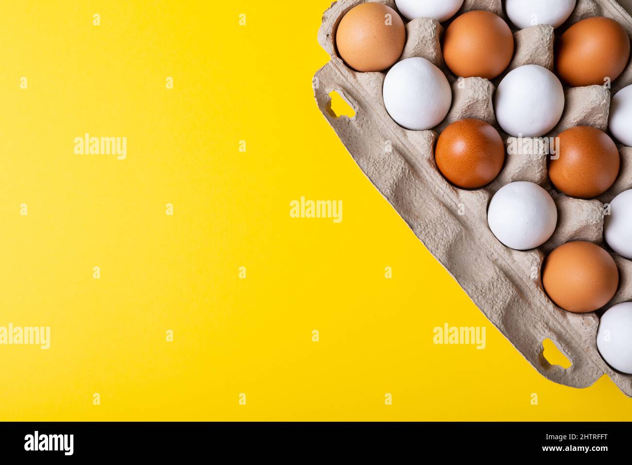 Overhead view of brown and white eggs in egg carton on yellow