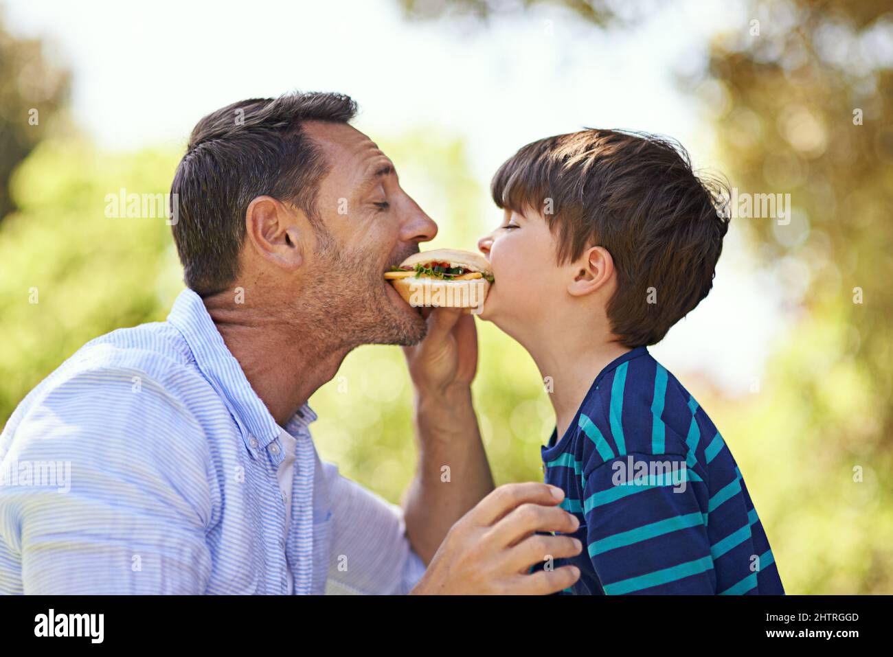 Whos got the biggest bite. Shot of a father and son biting into a sandwich at the same time. Stock Photo