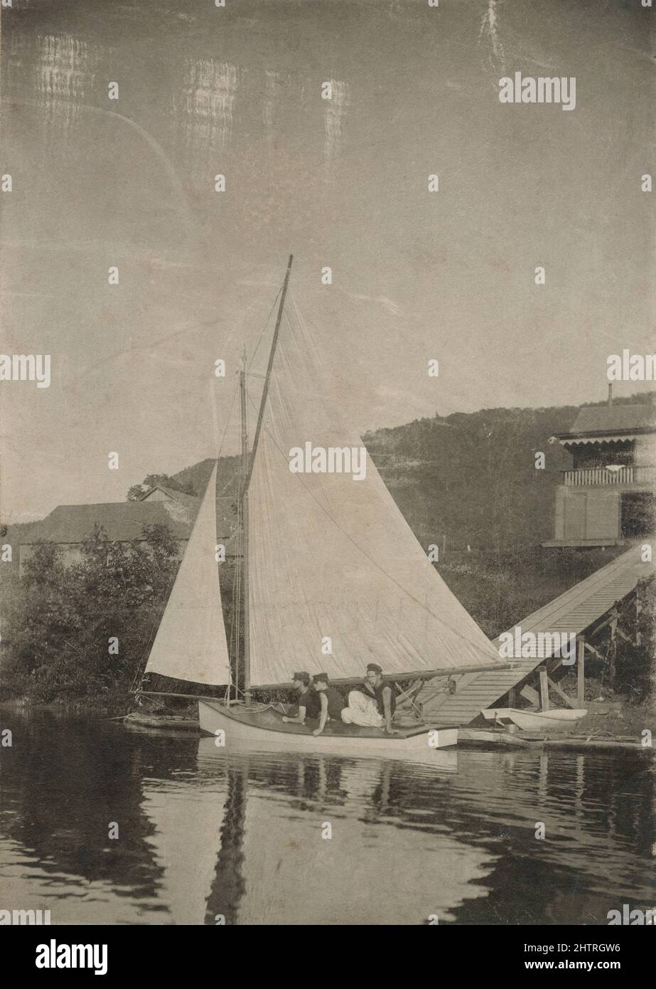Antique circa 1890 photograph, three boys on a sprit rig sailboat in front of a lake house. Exact location unknown, probably New England, USA. SOURCE: ORIGINAL PHOTOGRAPH Stock Photo