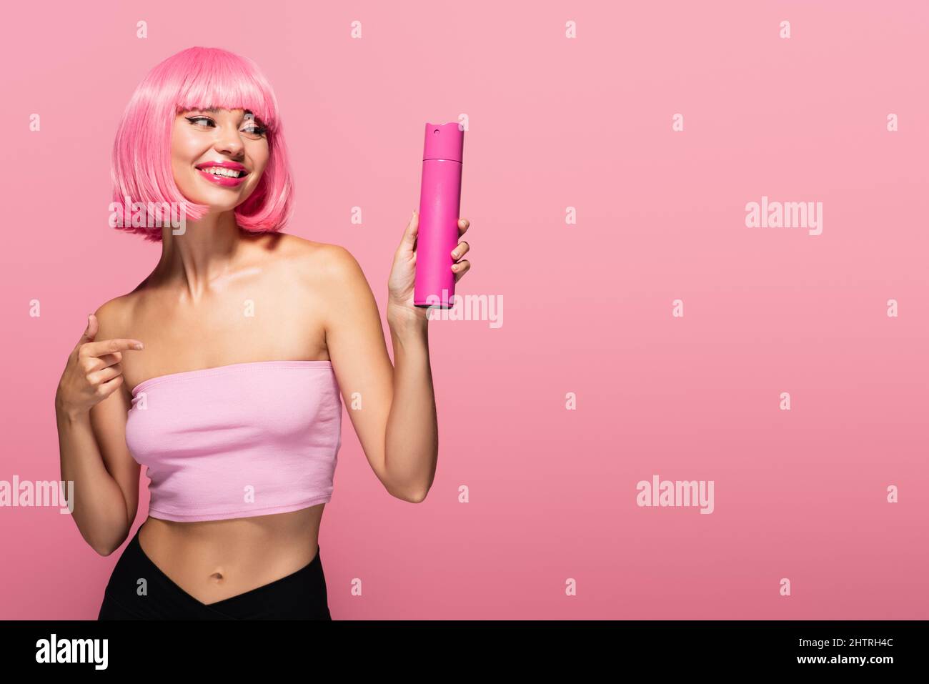 cheerful woman with colored hair pointing at bottle with spray isolated on pink,stock image Stock Photo