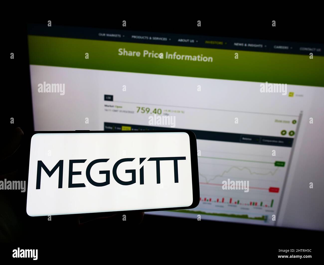 Person holding mobile phone with logo of British aerospace company Meggitt plc on screen in front of business web page. Focus on phone display. Stock Photo