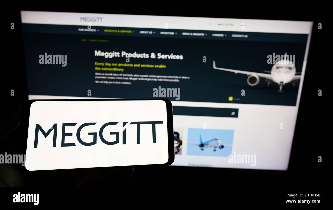 Person holding cellphone with logo of British aerospace company Meggitt plc on screen in front of business webpage. Focus on phone display. Stock Photo