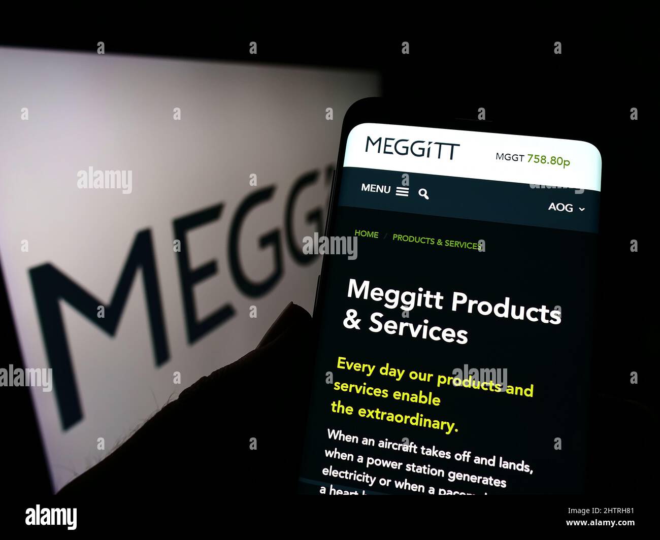Person holding cellphone with webpage of British aerospace company Meggitt plc on screen in front of logo. Focus on center of phone display. Stock Photo