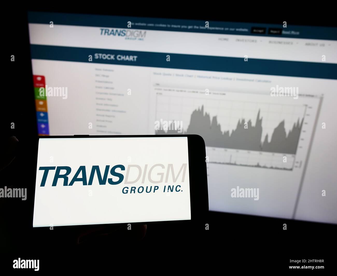 Person holding mobile phone with logo of American aerospace company TransDigm Group Inc. on screen in front of web page. Focus on phone display. Stock Photo