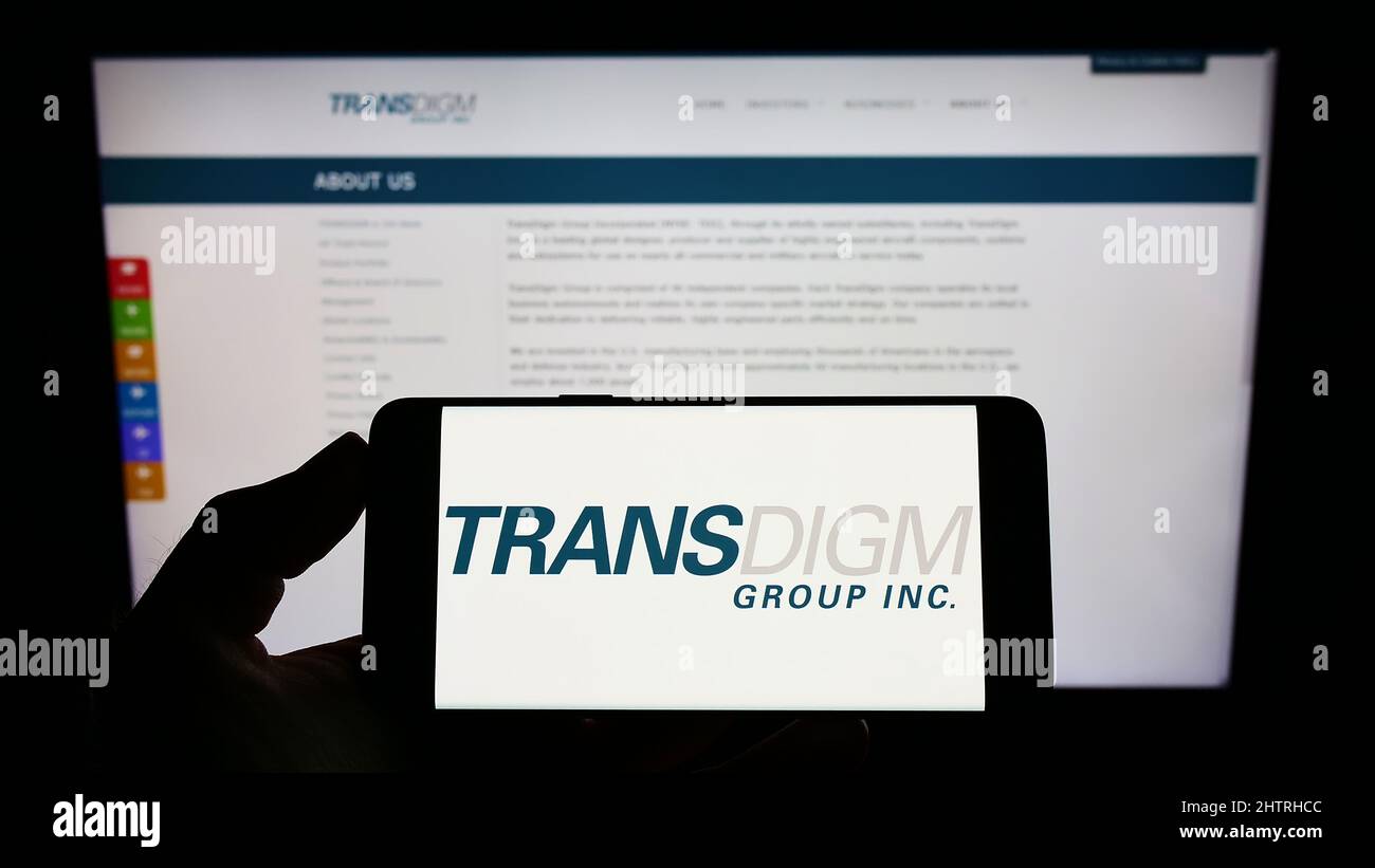 Person holding cellphone with logo of US aerospace company TransDigm Group Inc. on screen in front of business webpage. Focus on phone display. Stock Photo