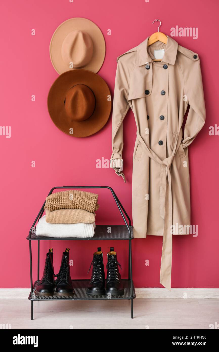 Shoes stand with warm clothes, hats and trenchcoat hanging on pink wall Stock Photo Alamy