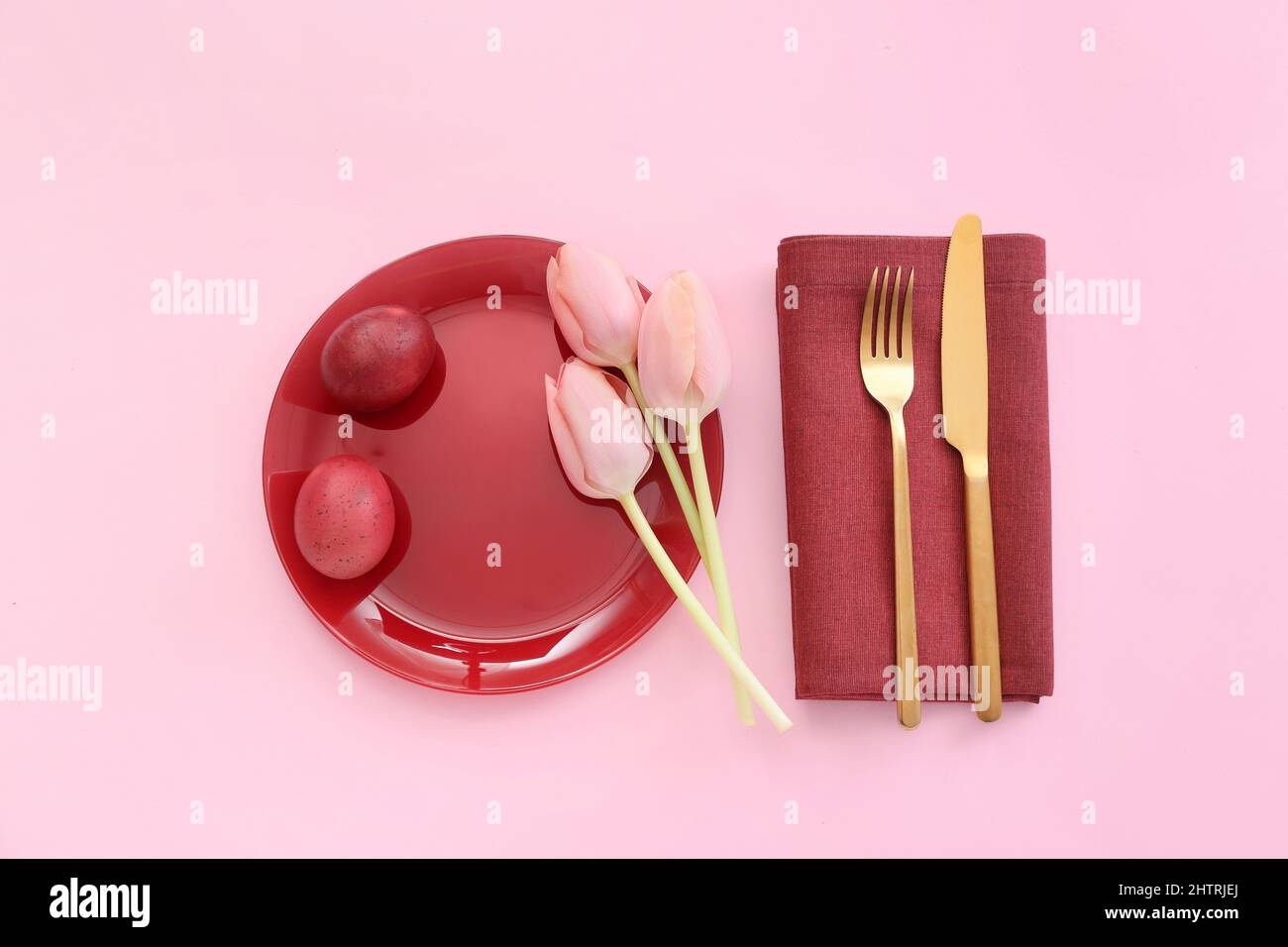 Beautiful table setting with red Easter eggs and tulips on pink background Stock Photo