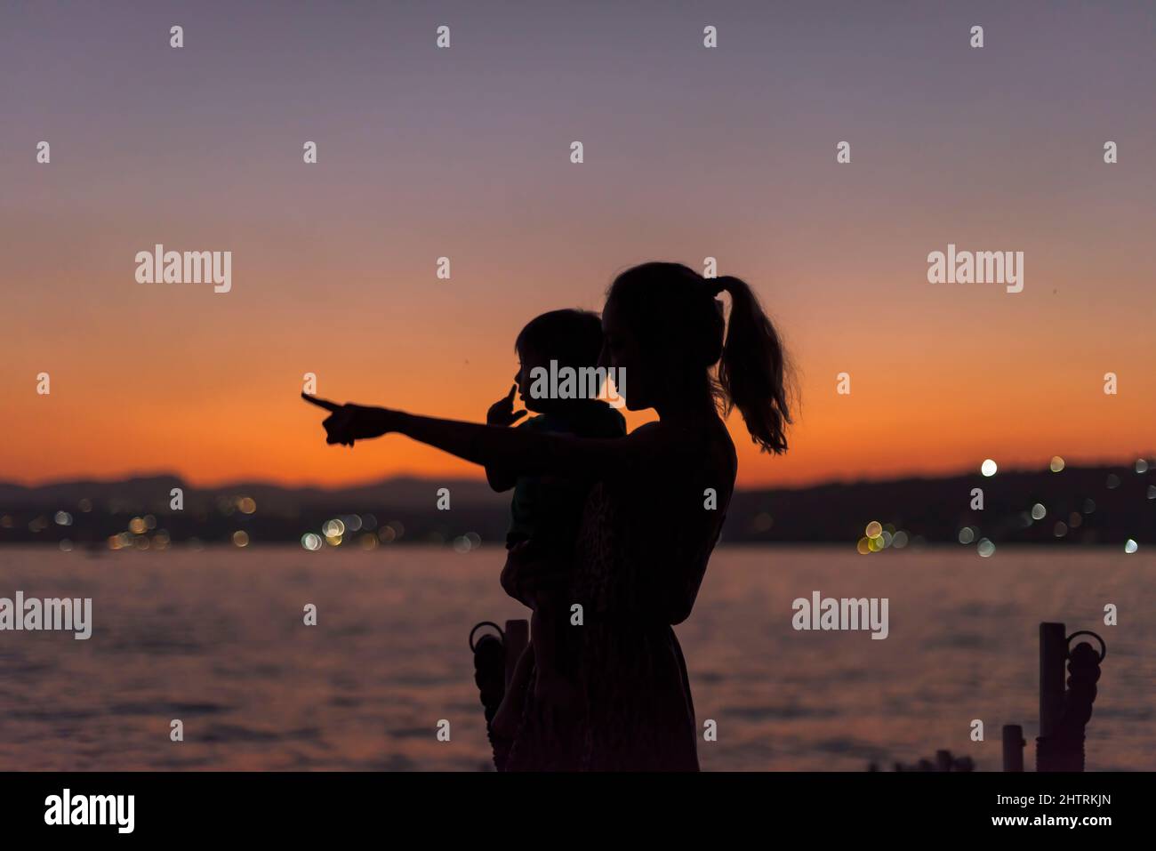Silhouette of a baby boy and his mom pointing to the horizon at dusk Stock Photo