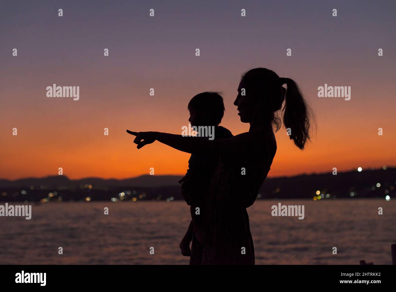 Silhouette of a Mom and a baby boy pointing to the horizon at dusk Stock Photo