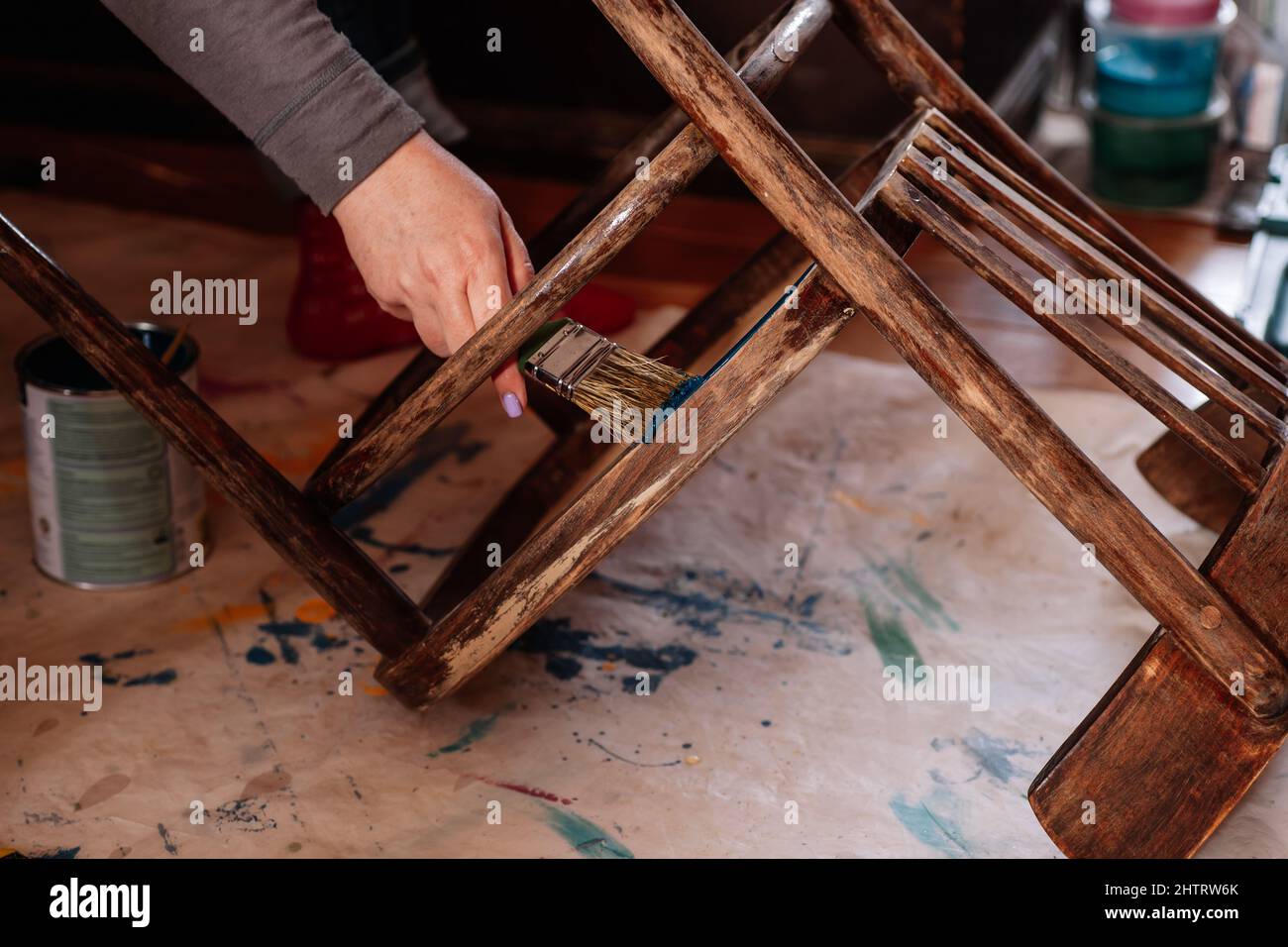 Lady hand having brush painting bottom of aged chair in blue collar in home workshop for furniture reinvention. Reuse of old things. Thinking about Stock Photo