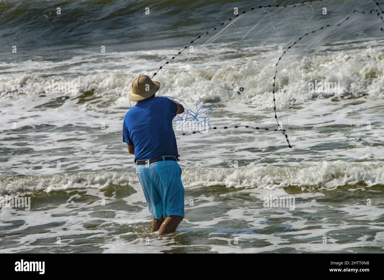 Fisherman throwing a cast net into the ocean with foamy waves at
