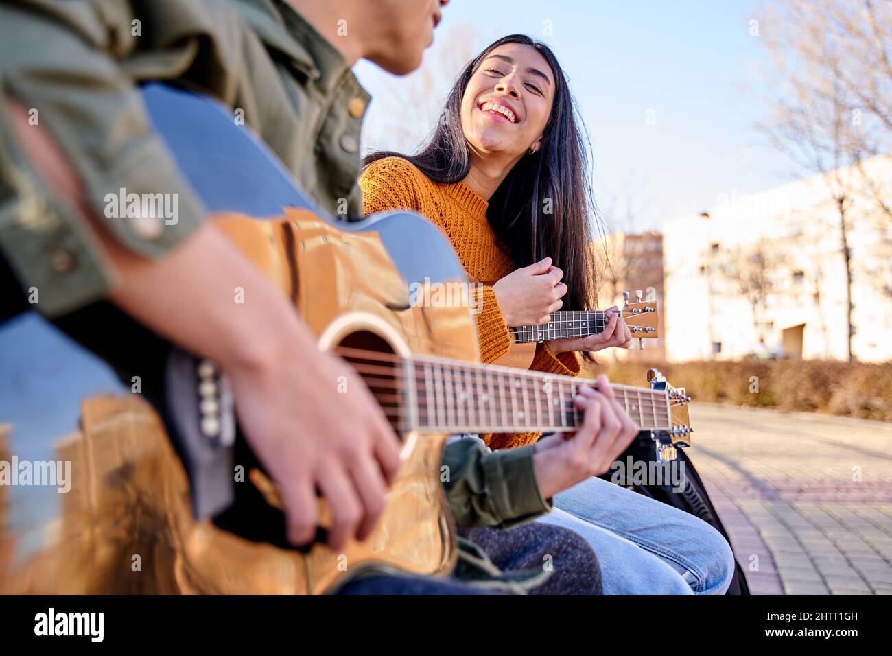 Two young friends have fun playing guitar together outdoors. couple