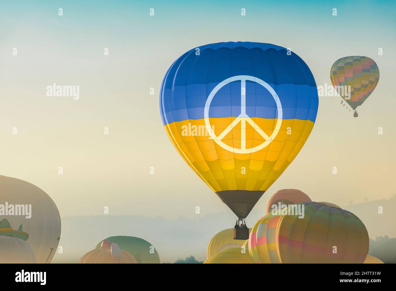 A hot air balloon starts its flight in the early morning, the fog is over the nature.   On the balloon are the national colors of Ukraine and a symbol Stock Photo