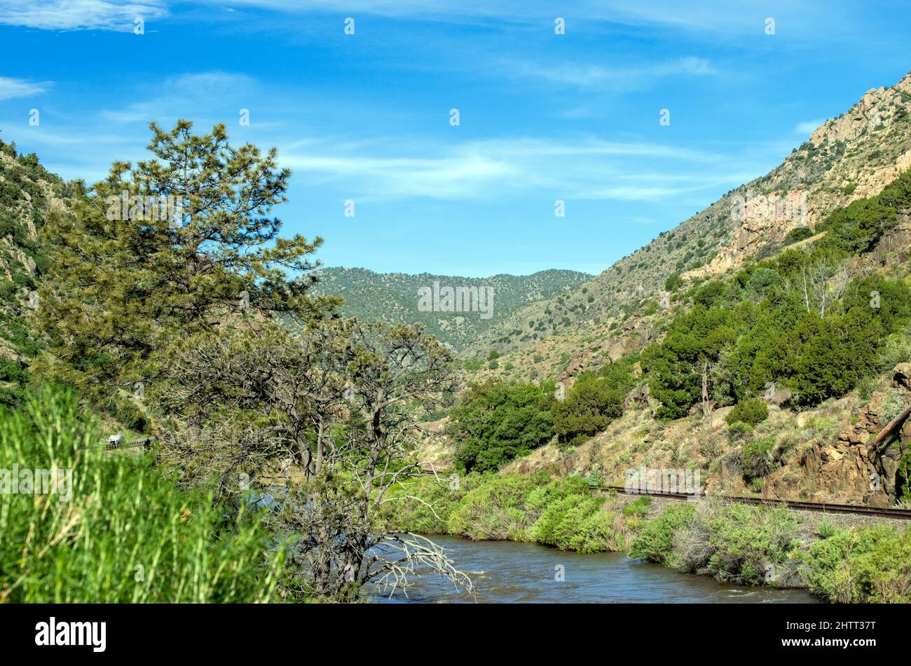 A picturesque mountain scene with gently rolling waters and a railroad track on a warm day in Colorado. Stock Photo