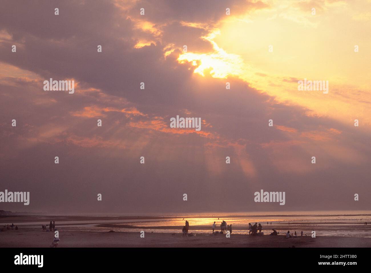 Sunbeams over Cabourg, Normandy coast,.Sunset over the Atlantic Ocean. Sun behind dark clouds. Silhouettes of people on beach. Cote Fleurie, France Stock Photo