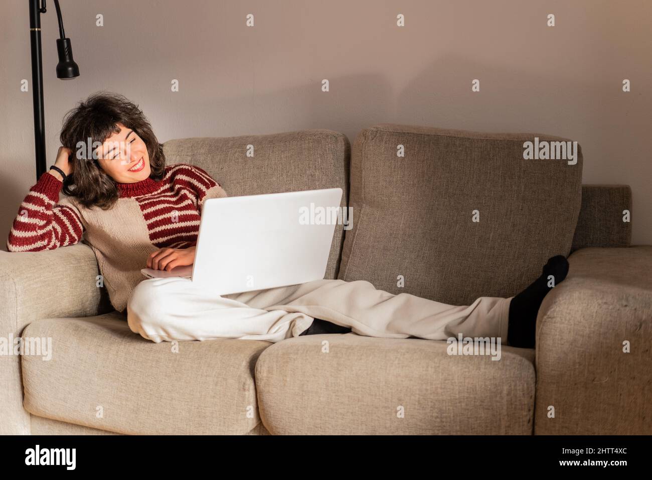 A young brunette woman in watching a movie on her computer lying on her sofa in her living room at home Stock Photo
