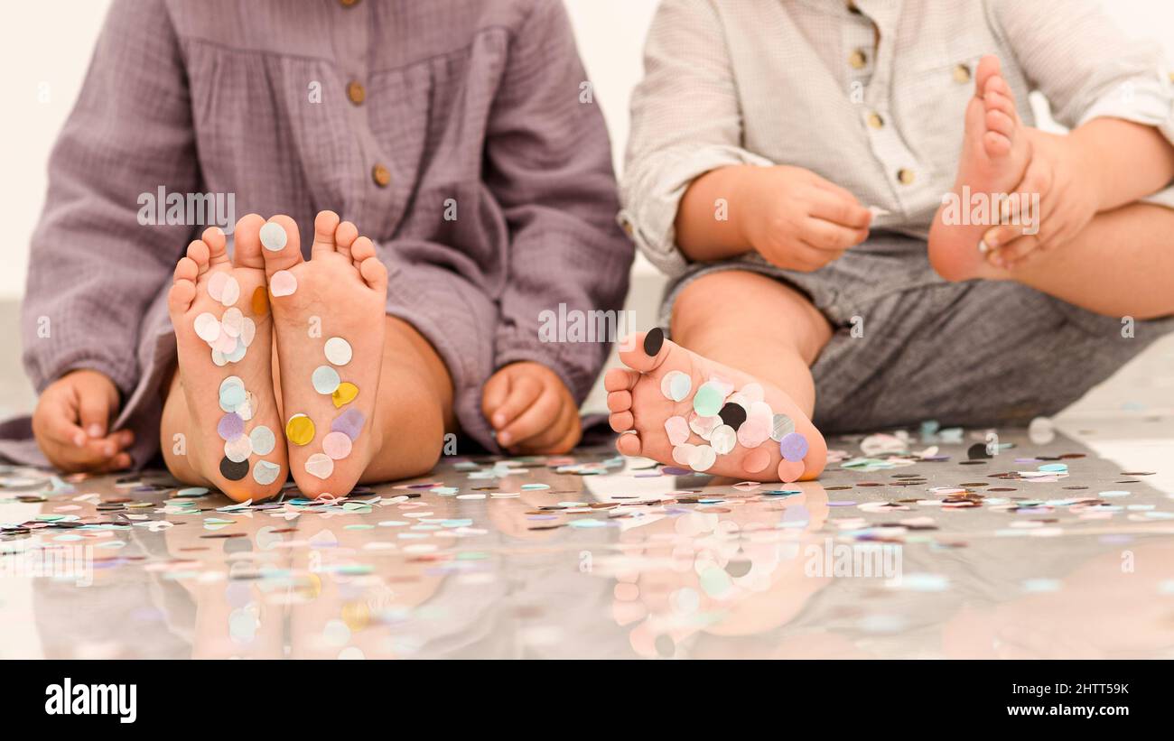 Happy kids having fun at a party. Little children's feet are covered in colorful non-biodegradable confetti. Unsustainable, microplastics pollution, environmental impact concept. Selective focus. Stock Photo