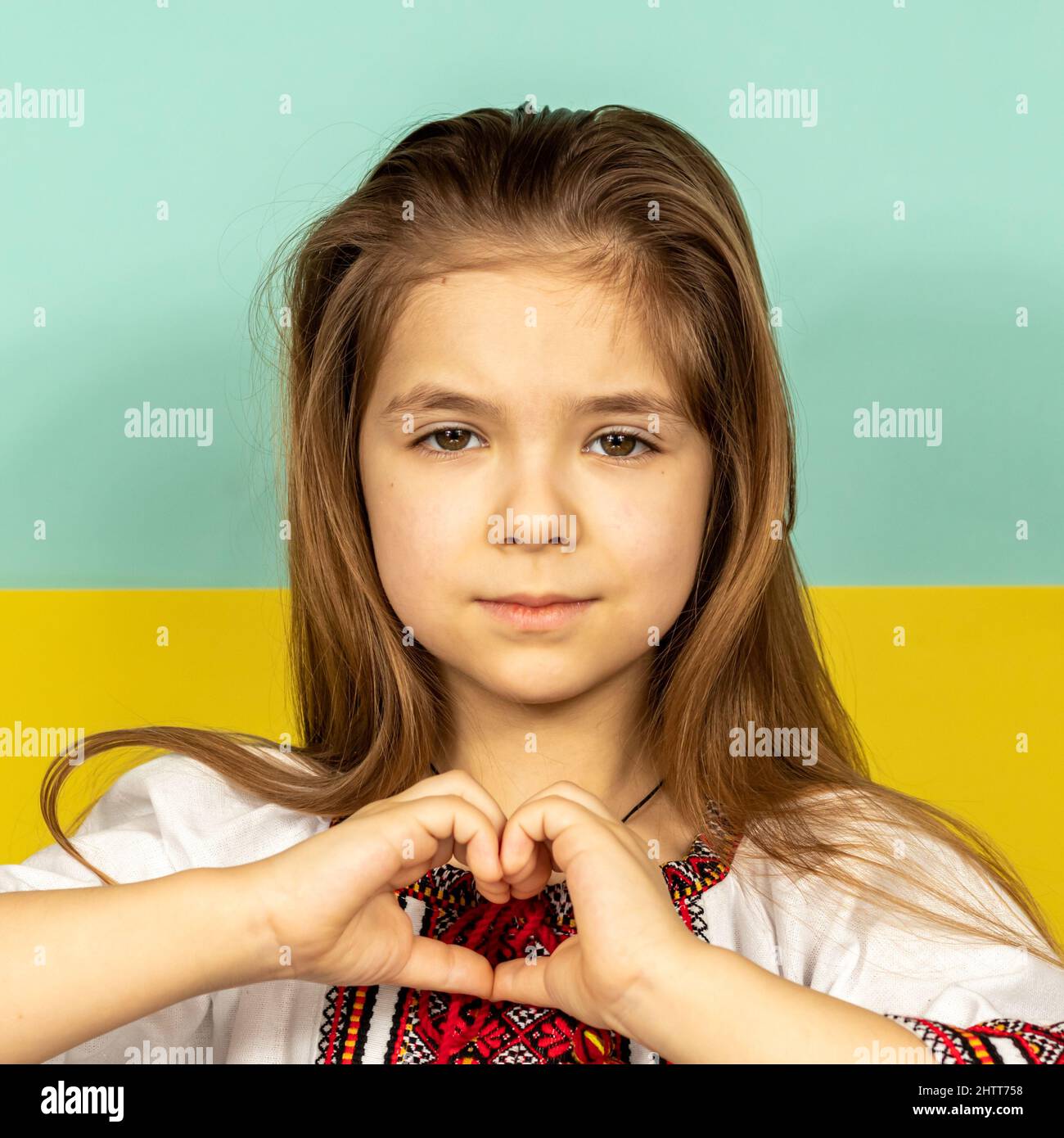 Close-up of a smiling girl in national Ukrainian clothes, vyshyvanka, shows hearts as a sign of love for Ukraine against the background of the Stock Photo