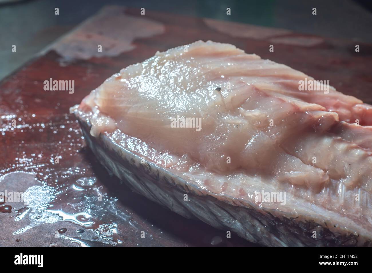 How to scrape tilapia fish using a knife,man wiping a fish on a wooden table. Stock Photo