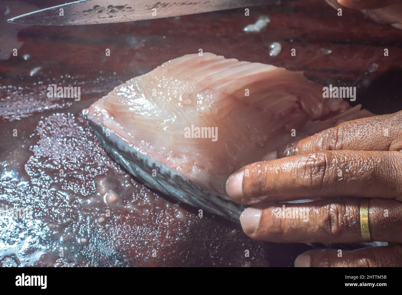 How to scrape tilapia fish using a knife,man wiping a fish on a wooden table. Stock Photo