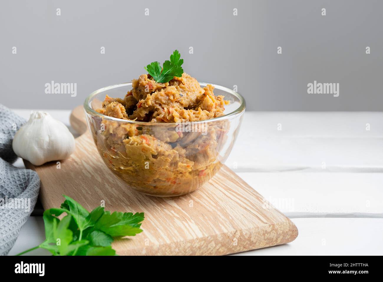 Traditional Balkan dish Kiopoolu, eggplant based spread in a glass bowl on wooden cutting board on white table with copy space Stock Photo