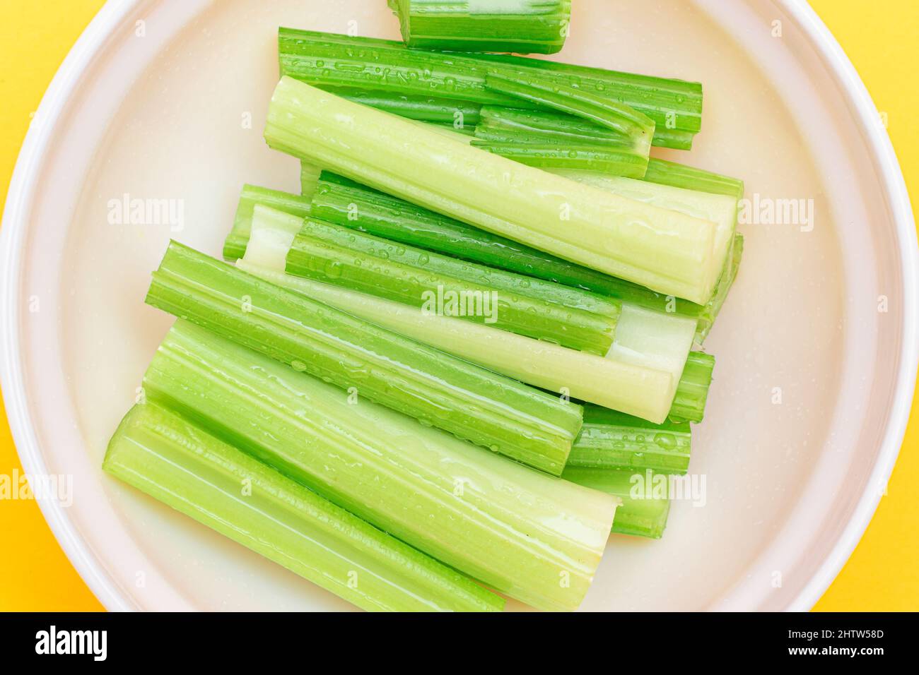 Fresh Chopped Celery Sticks with Water Drops in White Bowl Top View