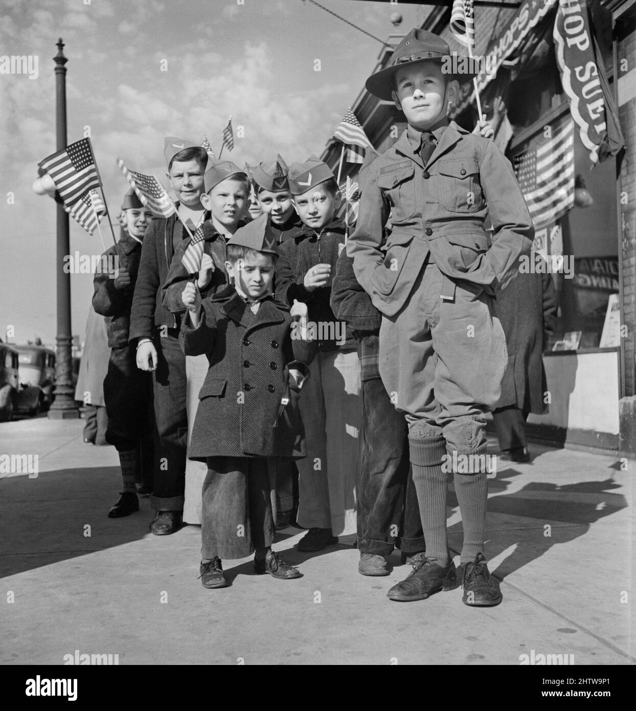 Boy Scout leading group of Young boys wearing garrison caps and holding American Flags at start of Parade and Flag Dedication Ceremony at Office of Civil Defense Headquarters, Chicago, Illinois, USA, Jack Delano, U.S. Office of War Information/U.S. Farm Security Administration, November 11, 1942 Stock Photo