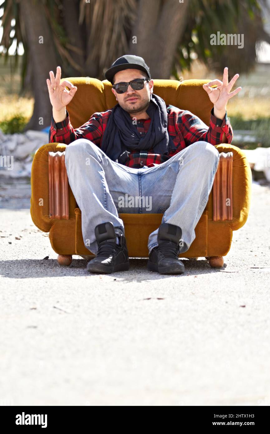 Sitting in style. A confident male sitting on a couch in the road holding up hand signs. Stock Photo