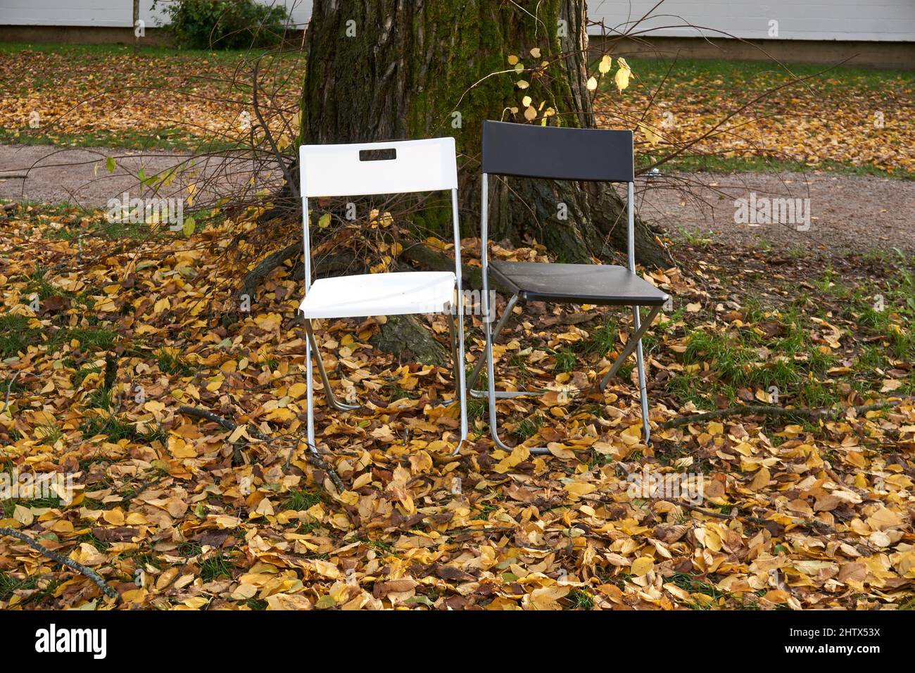 A black chair and a white chair sitting side by side outdoors Stock Photo