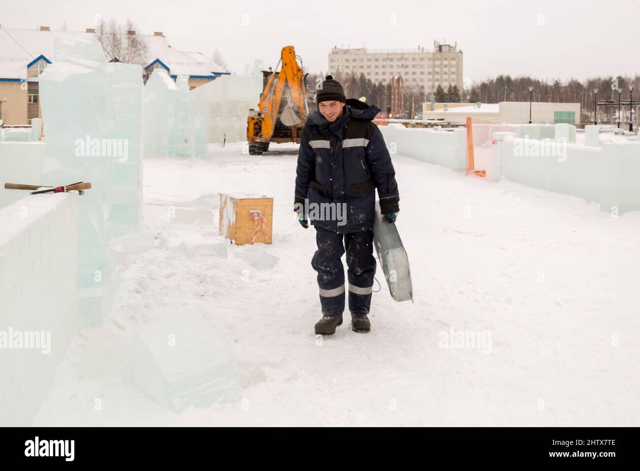 A working assembler in winter overalls with an iron trough walks along a construction site Stock Photo