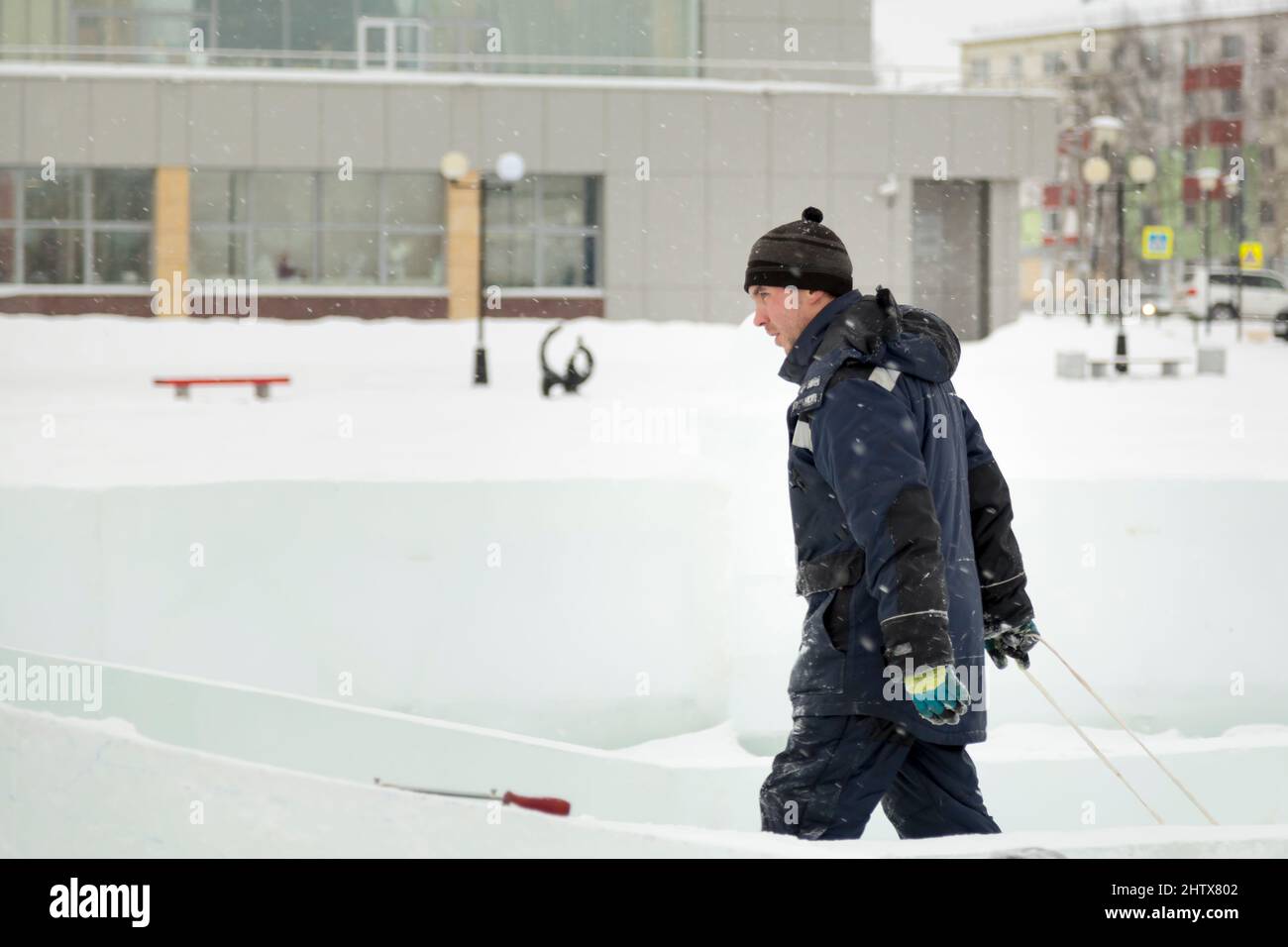 A working assembler in winter overalls with an iron trough walks along a construction site Stock Photo