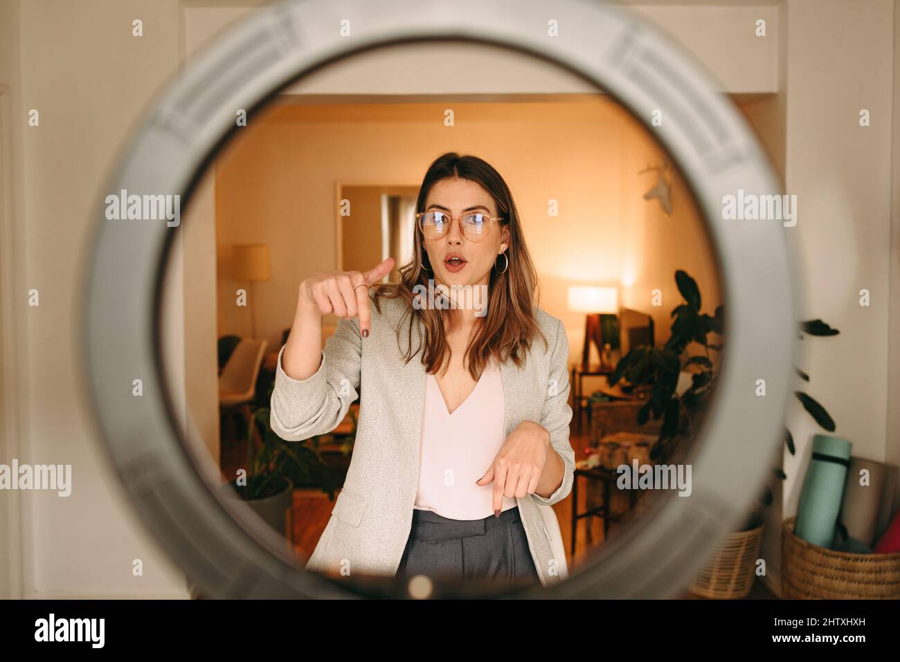 Click on the link below. Content creator pointing down while recording a video for her followers. Female influencer using a ring light to make a video Stock Photo