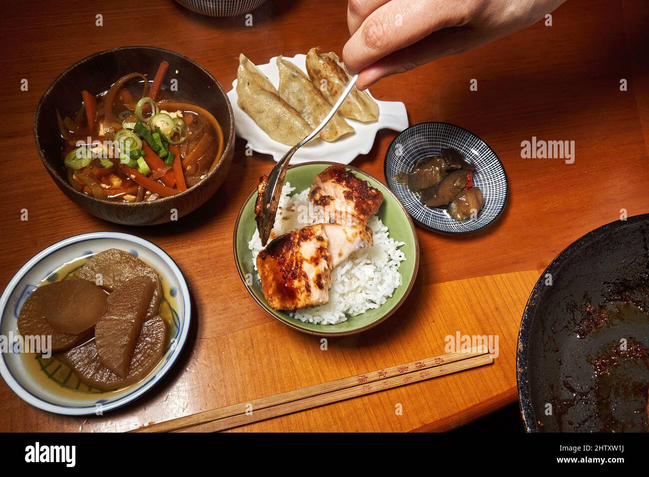 Hand with a spoon puts a piece of salmon fillet into a bowl of rice at a Japanese diner with many bowls Stock Photo