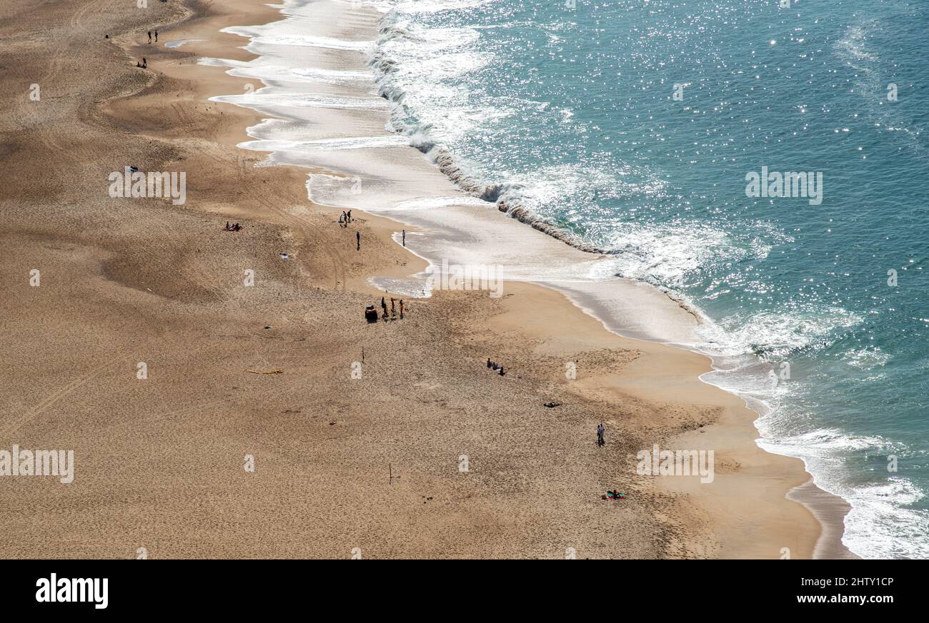 Two people walking alone on a sandy tropical beach. Nazare Portugal Stock Photo