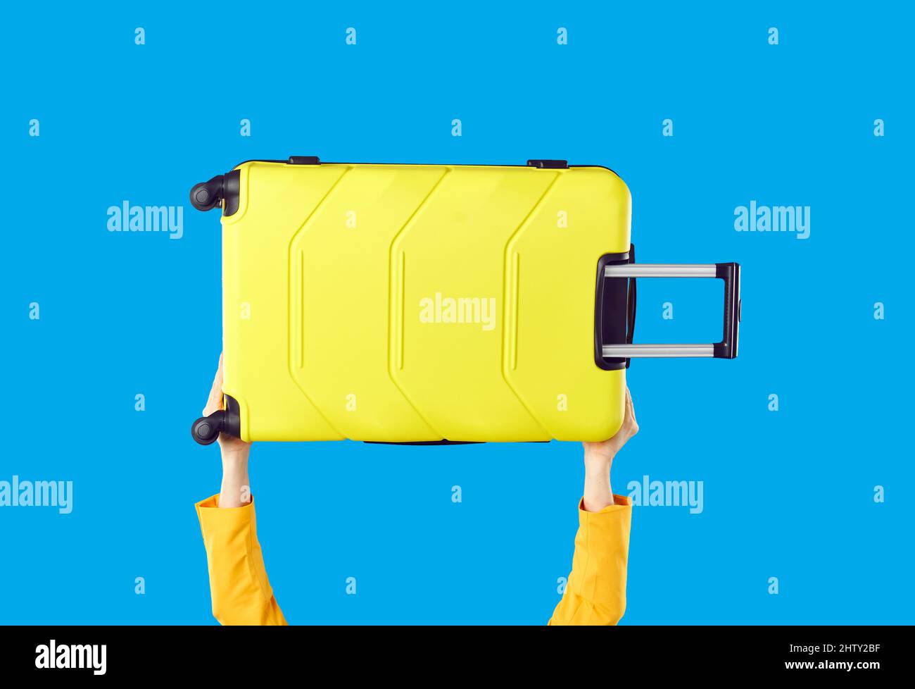 Female tourist holding her yellow wheeled suitcase isolated on blue colour background Stock Photo