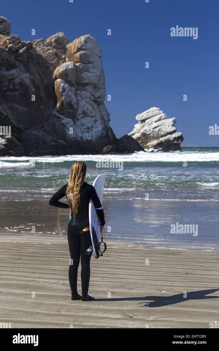 Portrait of Female Surfer With Surf Board and Black Wet Suit looking at Surf Waves on Morro Bay Beach, California Stock Photo