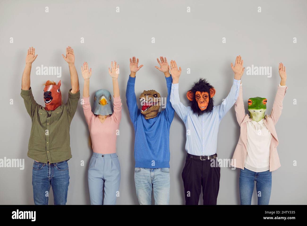 Team of young people in different funny animal masks standing together and raising their hands up Stock Photo